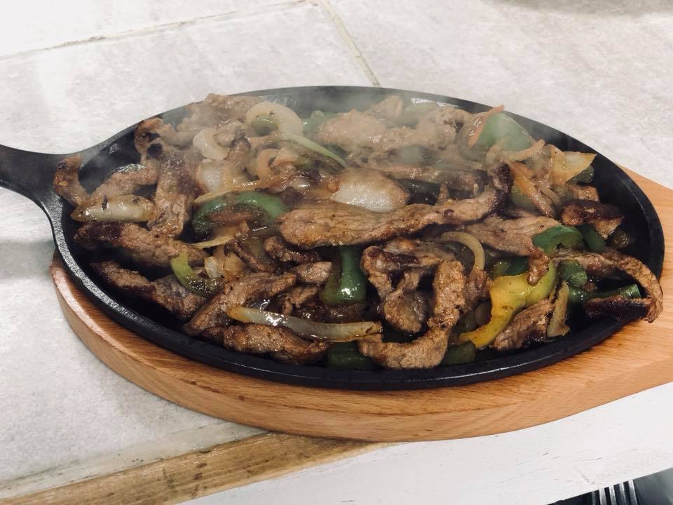 Sizzling steak fajitas with peppers and onions on a cast-iron skillet
