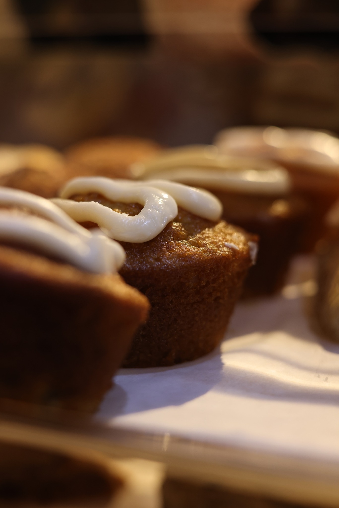 A row of golden house-made muffins topped with cream-cheese icing in the pastry case.